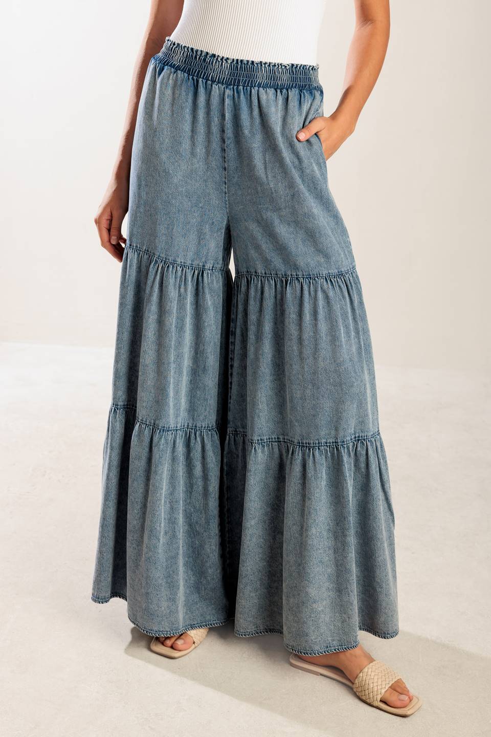 A wide-leg washed denim pant featuring a smocked waistband and tiered bottom.