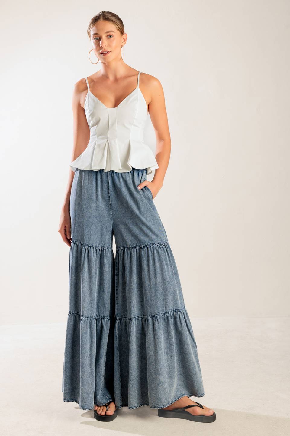 A wide-leg washed denim pant featuring a smocked waistband and tiered bottom.