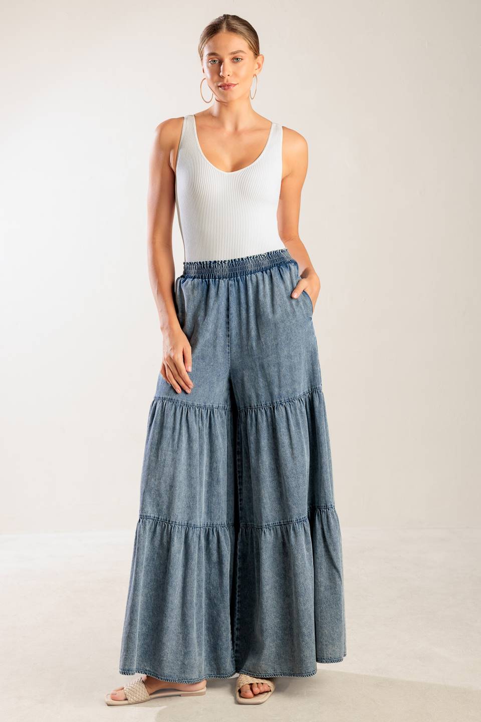 A wide-leg washed denim pant featuring a smocked waistband and tiered bottom.