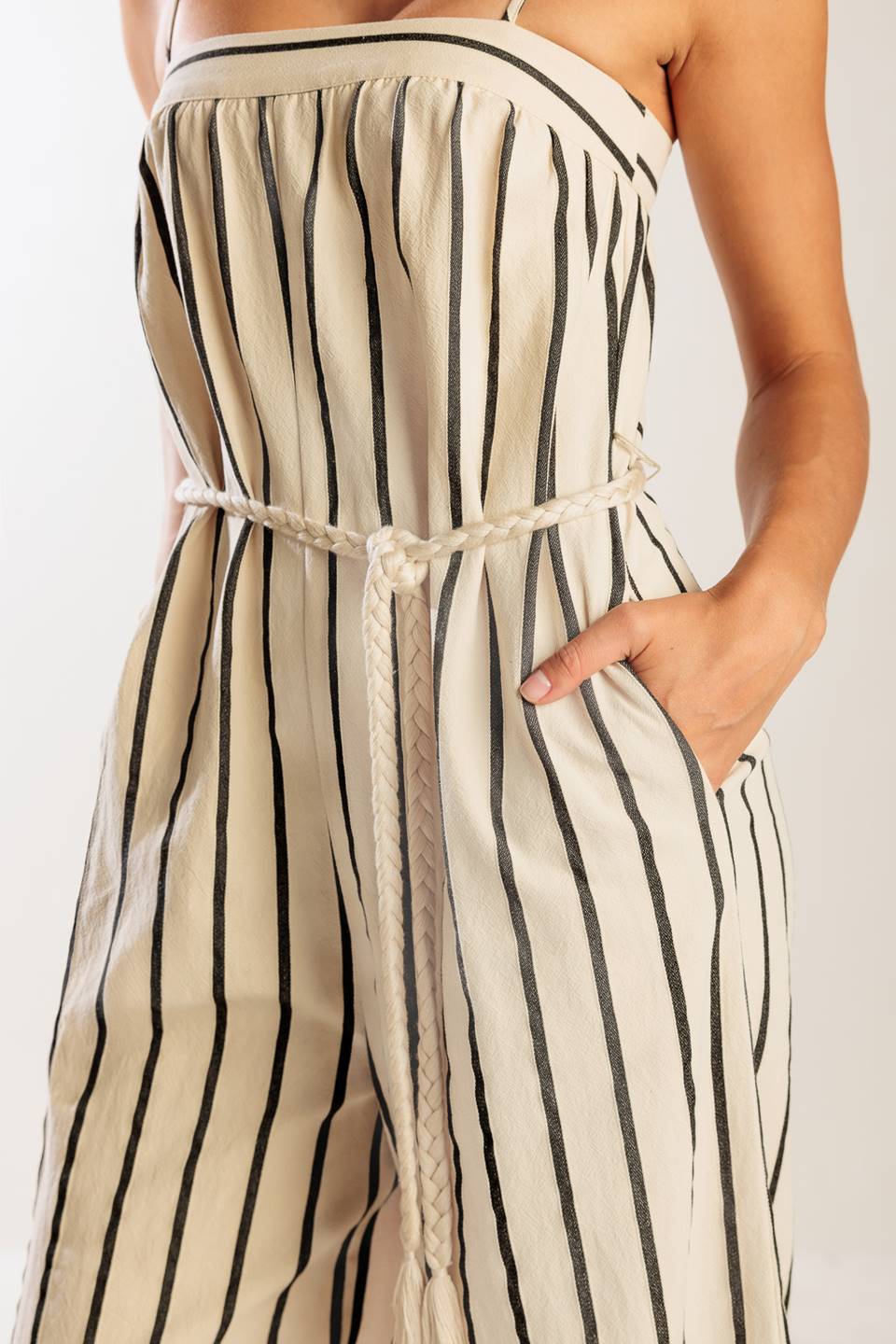 A striped woven jumpsuit featuring straight neckline, straps, side pockets, back closure and braided belt