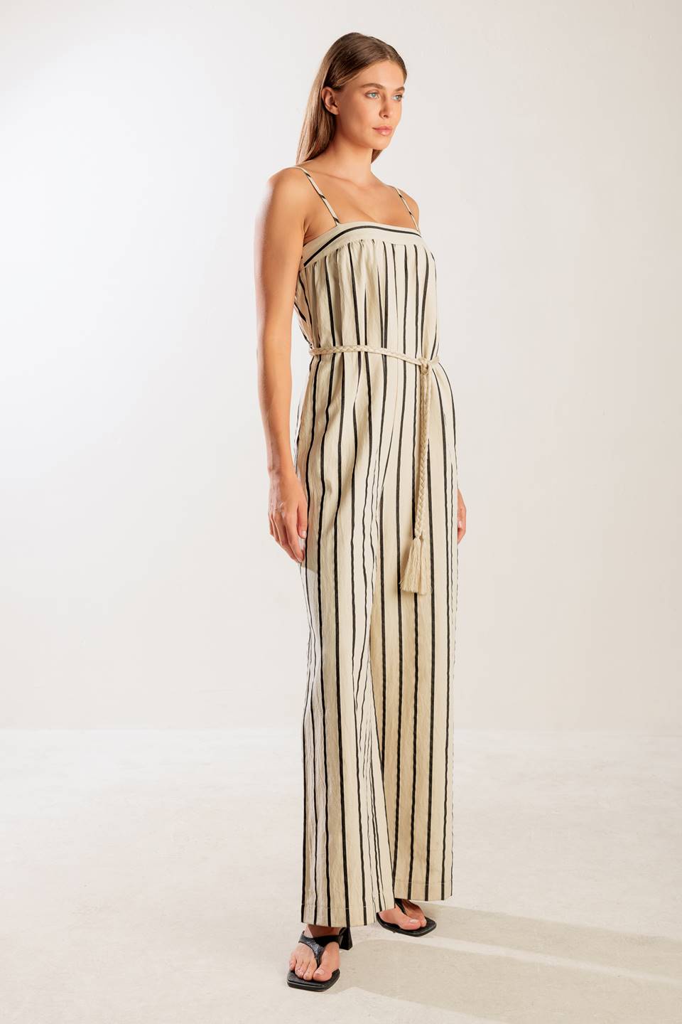 A striped woven jumpsuit featuring straight neckline, straps, side pockets, back closure and braided belt