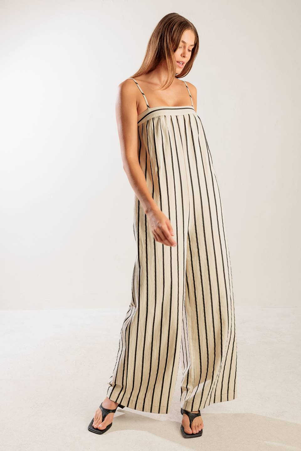 A striped woven jumpsuit featuring straight neckline, straps, side pockets, back closure and braided belt