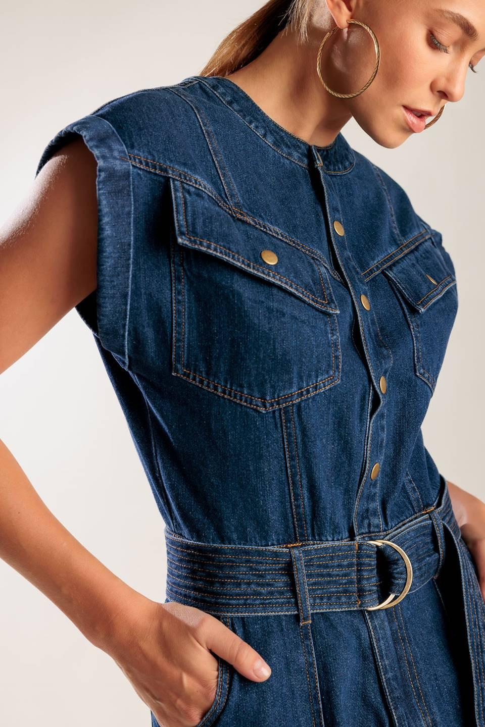 A denim romper featuring a round neckline, button down, cuffed sleeve, self belt, and pockets.