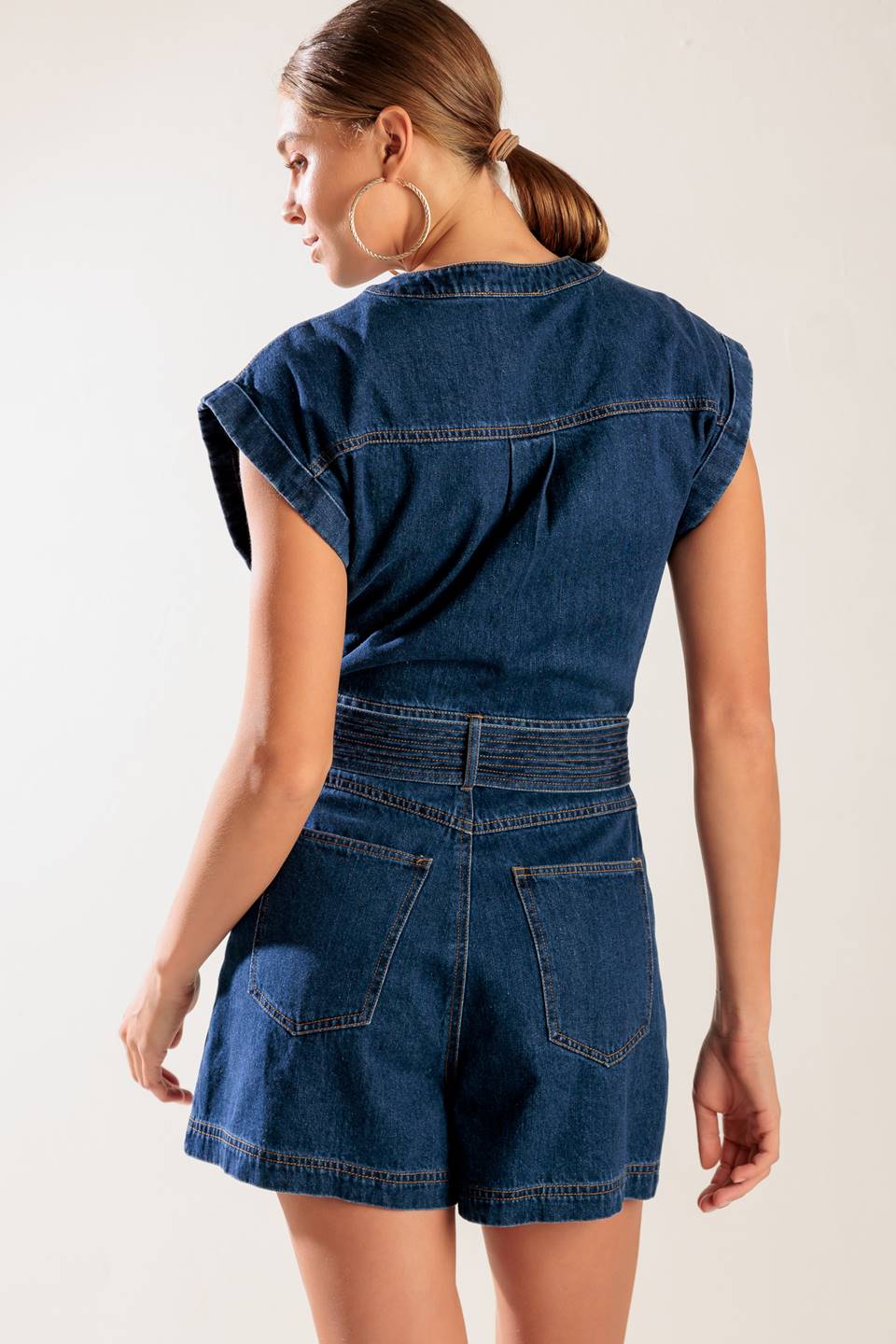 A denim romper featuring a round neckline, button down, cuffed sleeve, self belt, and pockets.