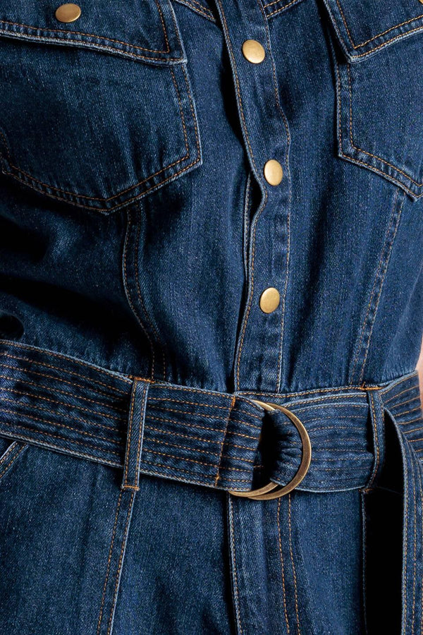 A denim romper featuring a round neckline, button down, cuffed sleeve, self belt, and pockets.