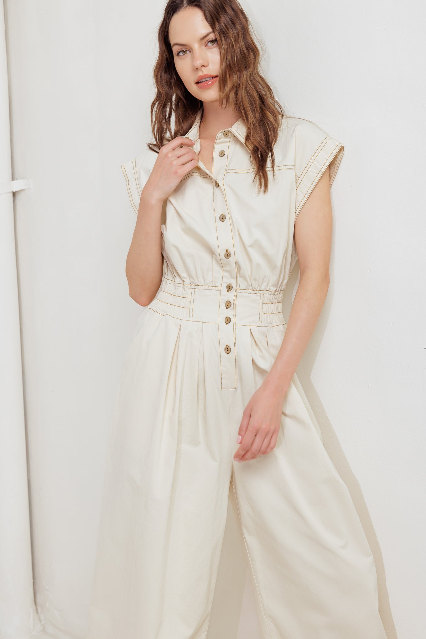 A solid woven jumpsuit featuring collar, dropped shoulder with short sleeve, button down, elasticized waistband, side pockets and wide leg