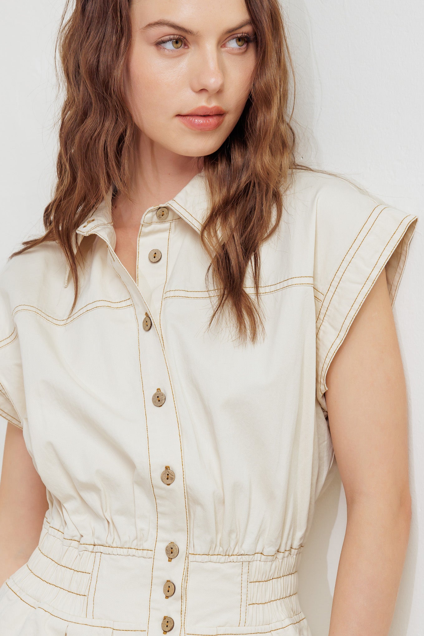 A solid woven jumpsuit featuring collar, dropped shoulder with short sleeve, button down, elasticized waistband, side pockets and wide leg