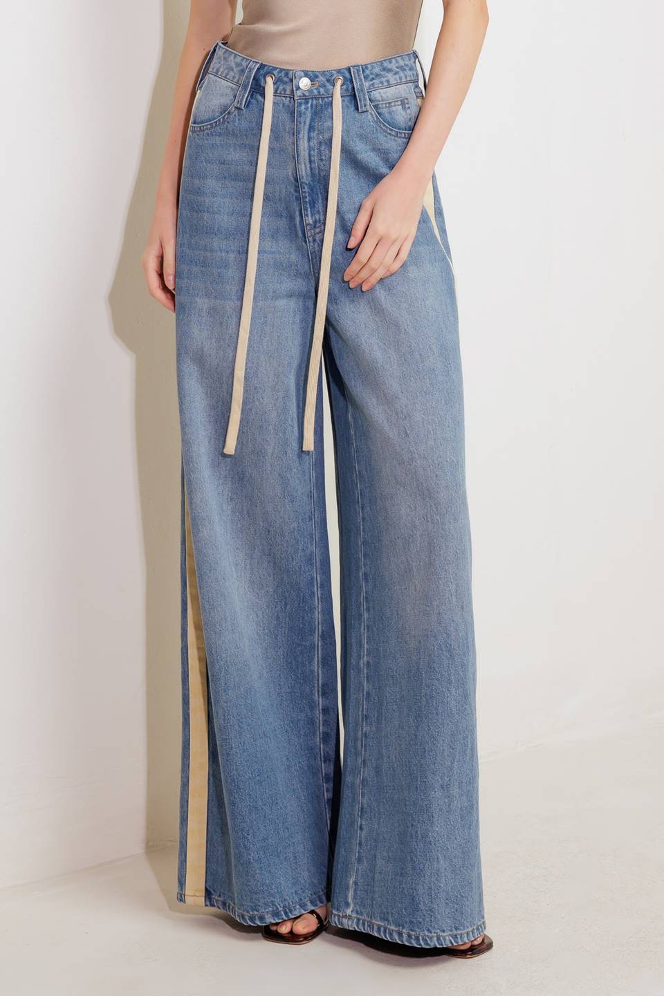 A washed denim pant featuring front closure, pockets, contrasting waist tie, side contrasting stripe and wide leg