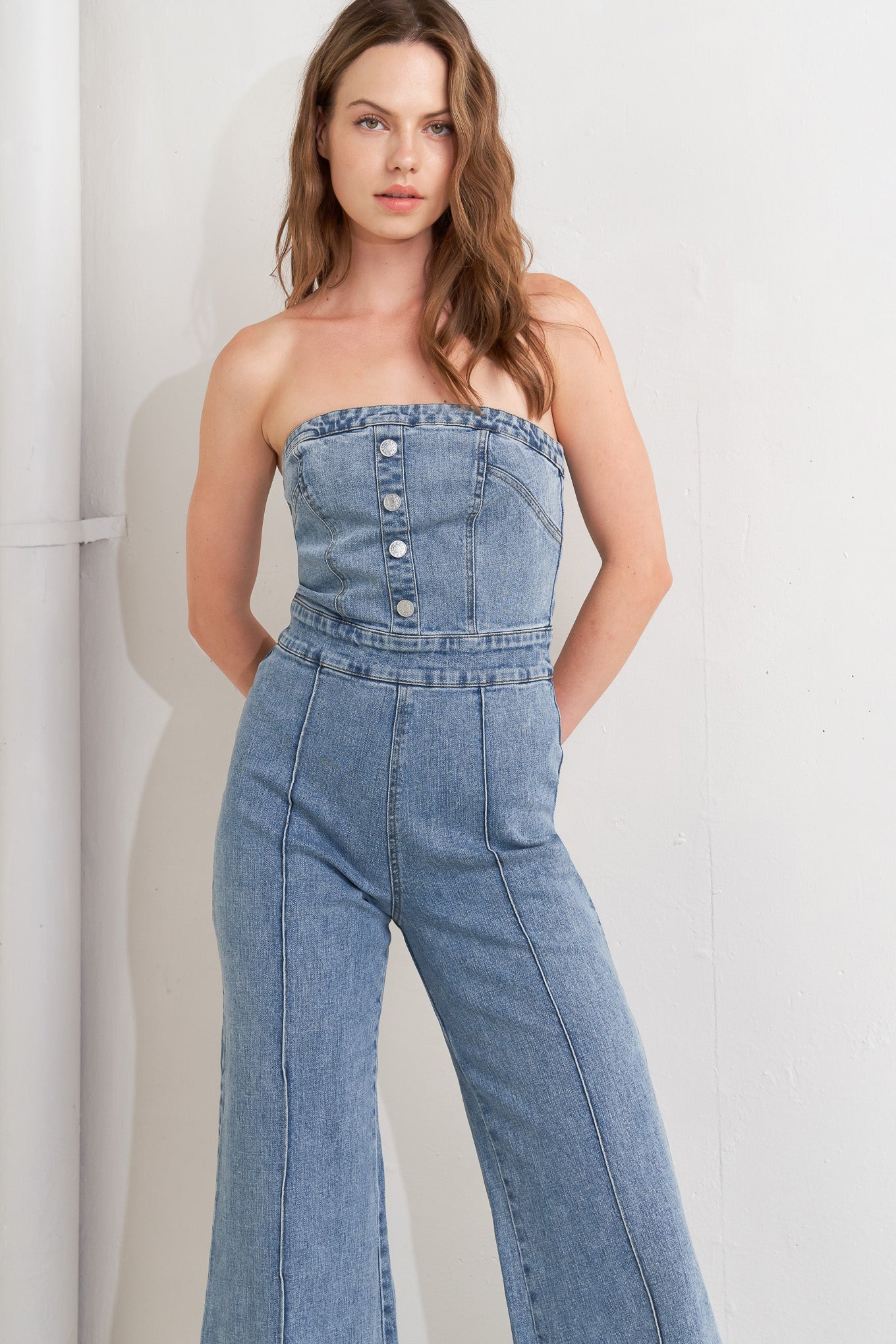 A washed denim jumpsuit featuring strapless, front button detail, wide leg and back zipper closure