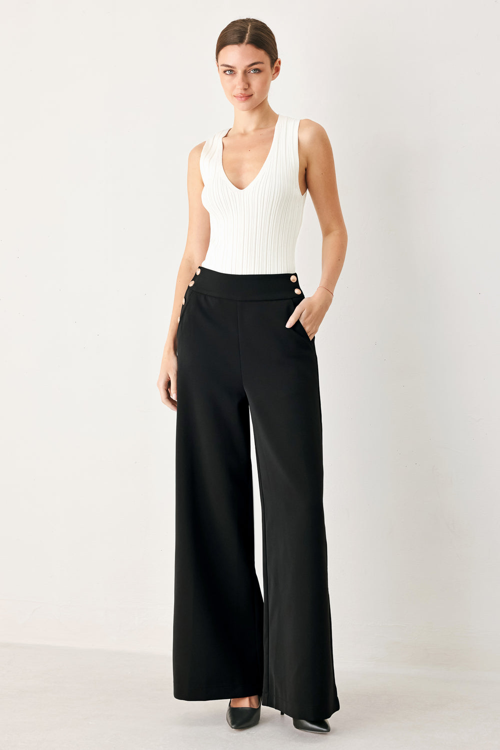 White wide-leg pants with gold buttons worn by a person on a white background