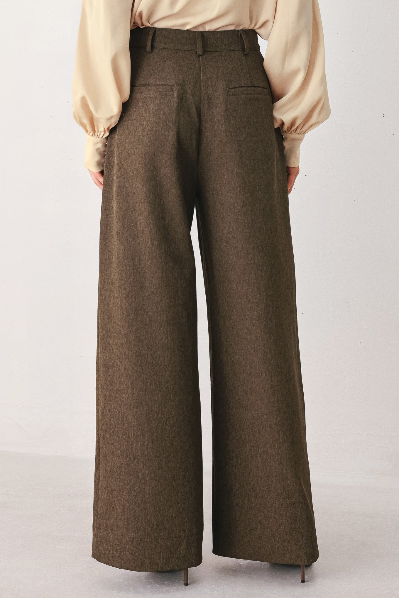 A woman wearing high-waisted, wide-leg brown trousers | FREEMARKET