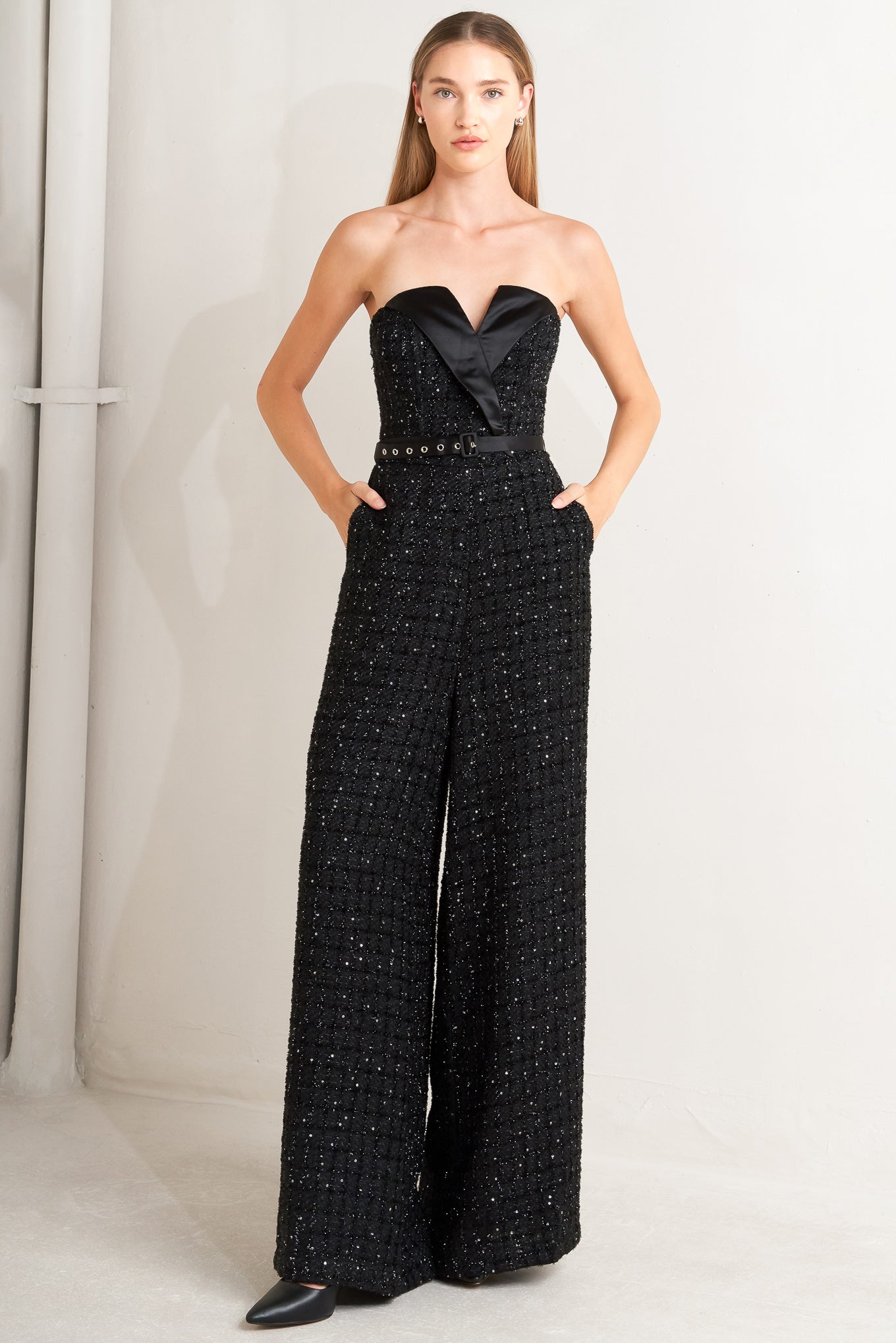 A woven tweed jumpsuit featuring strapless with V cut out, satin lapel, satin belt, wide leg and back zipper closure