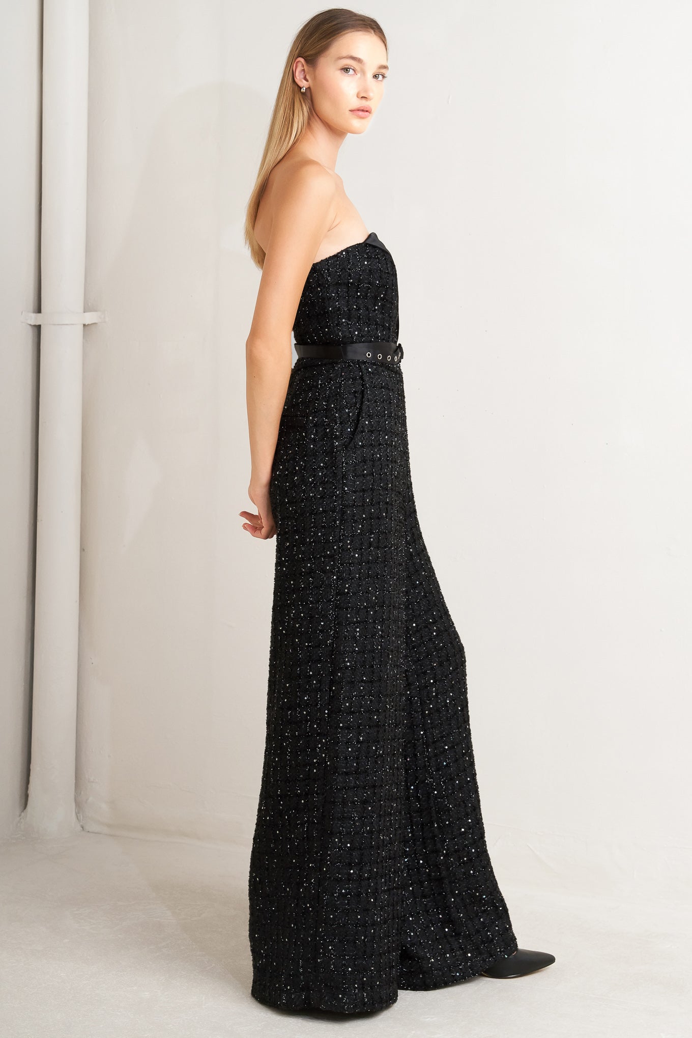 A woven tweed jumpsuit featuring strapless with V cut out, satin lapel, satin belt, wide leg and back zipper closure