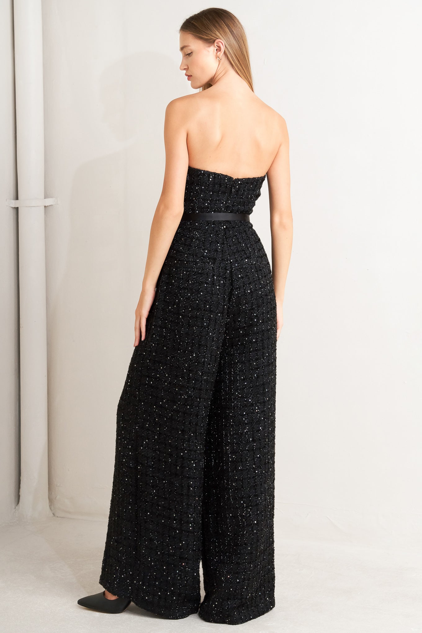 A woven tweed jumpsuit featuring strapless with V cut out, satin lapel, satin belt, wide leg and back zipper closure