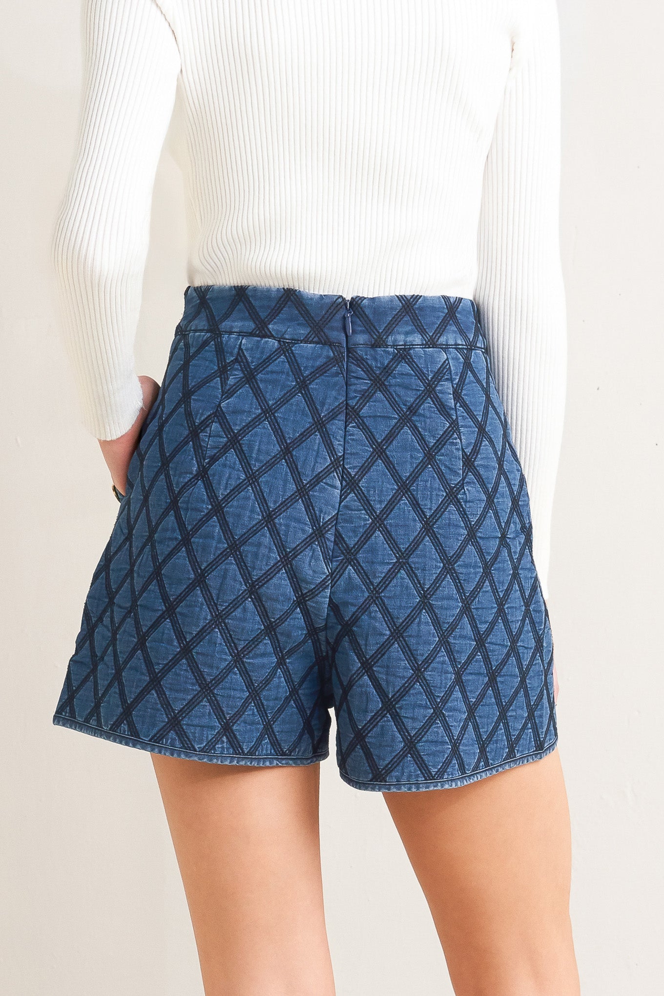 A quilted woven short featuring side pocket with button detail and back zipper closure.