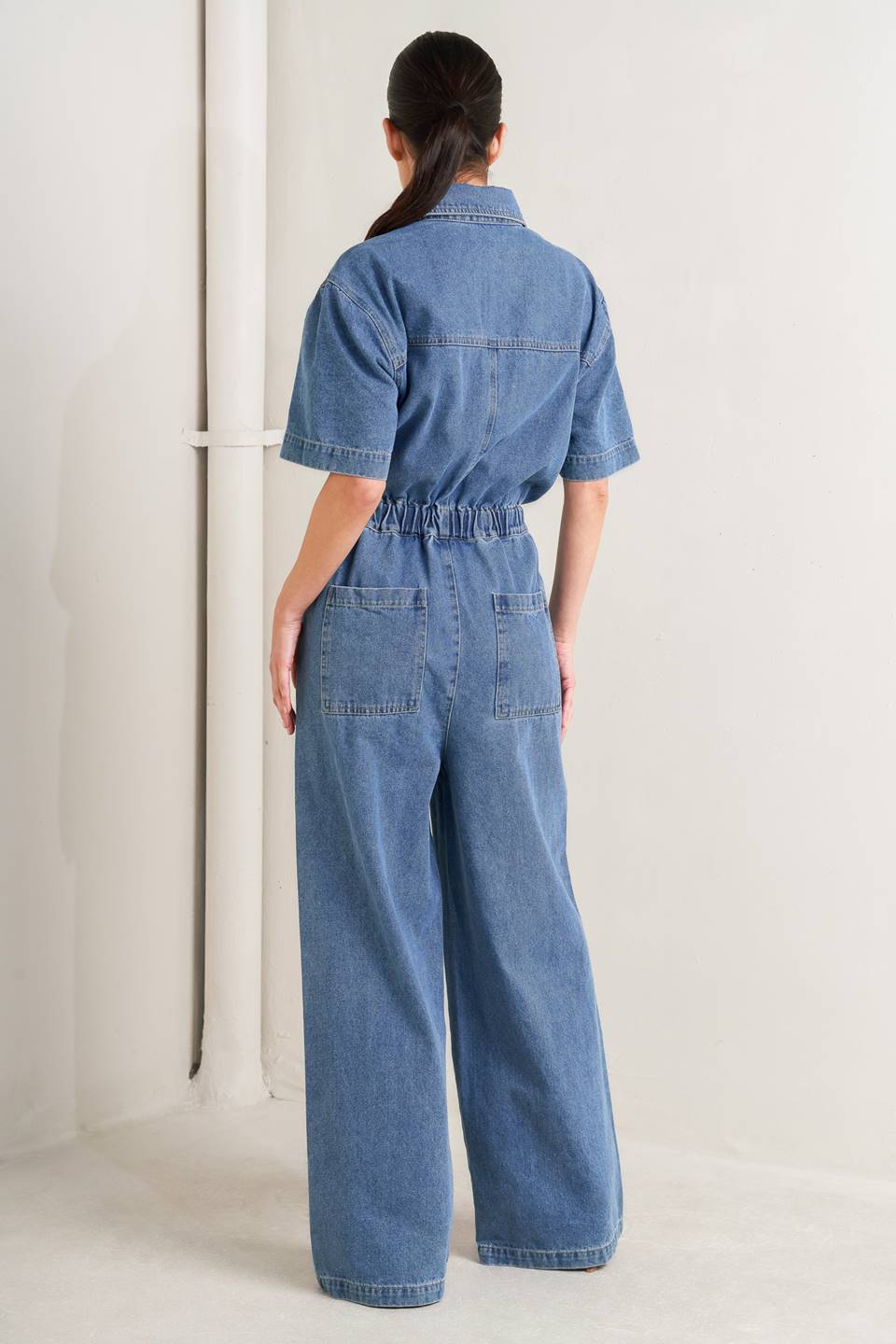 Woman wearing a denim jumpsuit against a plain background - FLYING TOMATO