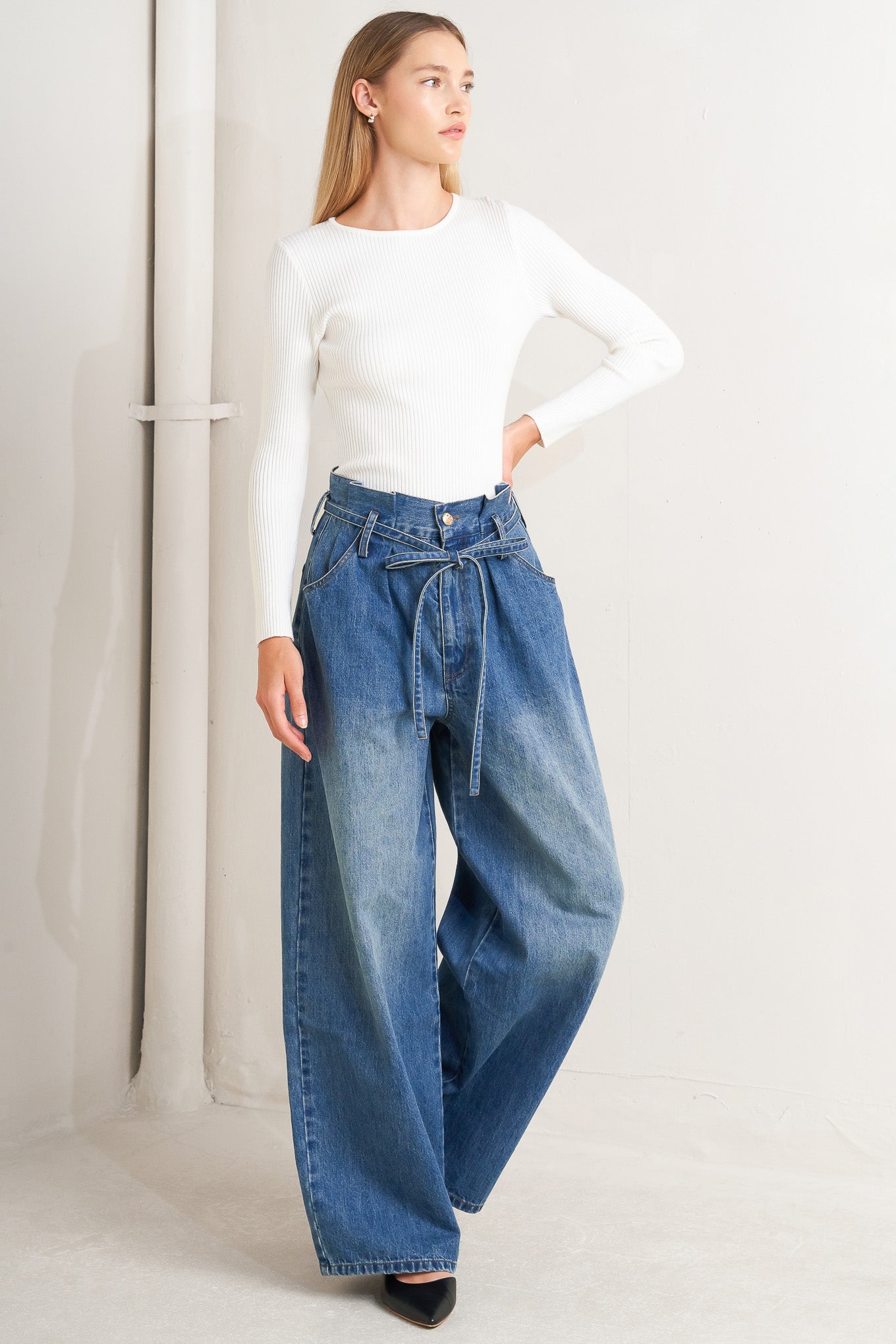 A washed denim pant featuring paper bag waist, front closure, skinny self sash tie, side/back pockets and balloon leg