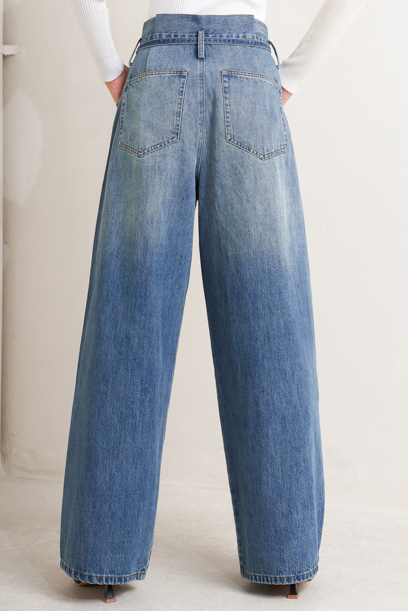A washed denim pant featuring paper bag waist, front closure, skinny self sash tie, side/back pockets and balloon leg