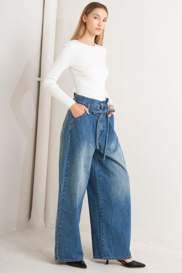 A washed denim pant featuring paper bag waist, front closure, skinny self sash tie, side/back pockets and balloon leg