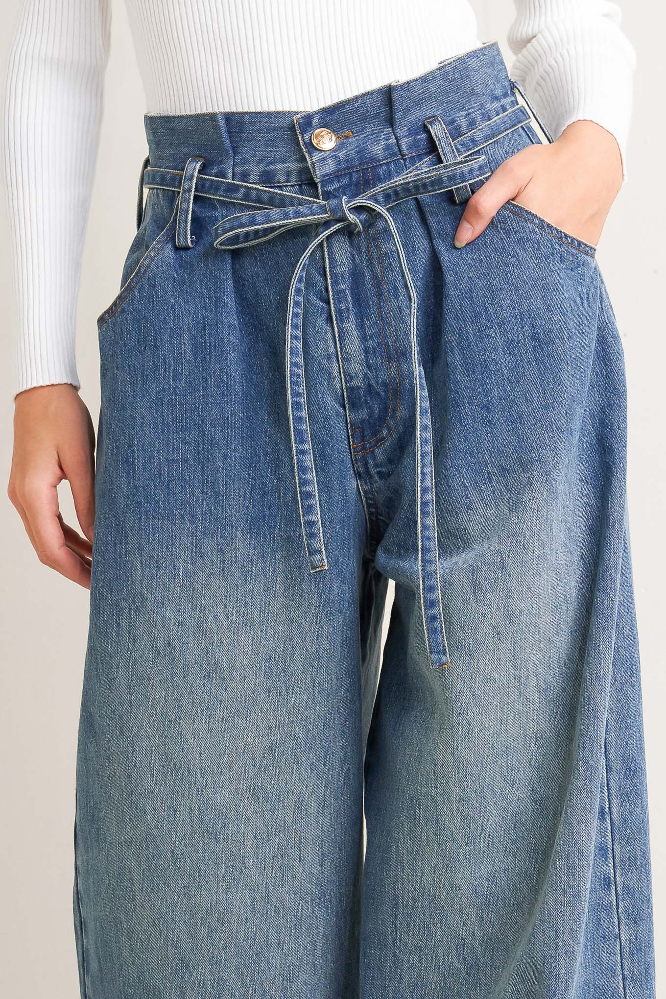 A washed denim pant featuring paper bag waist, front closure, skinny self sash tie, side/back pockets and balloon leg