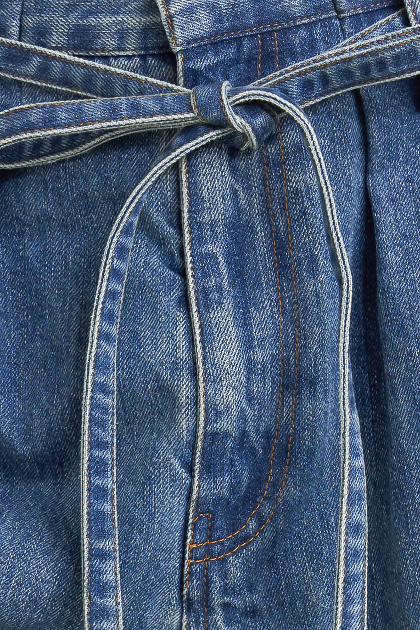 A washed denim pant featuring paper bag waist, front closure, skinny self sash tie, side/back pockets and balloon leg