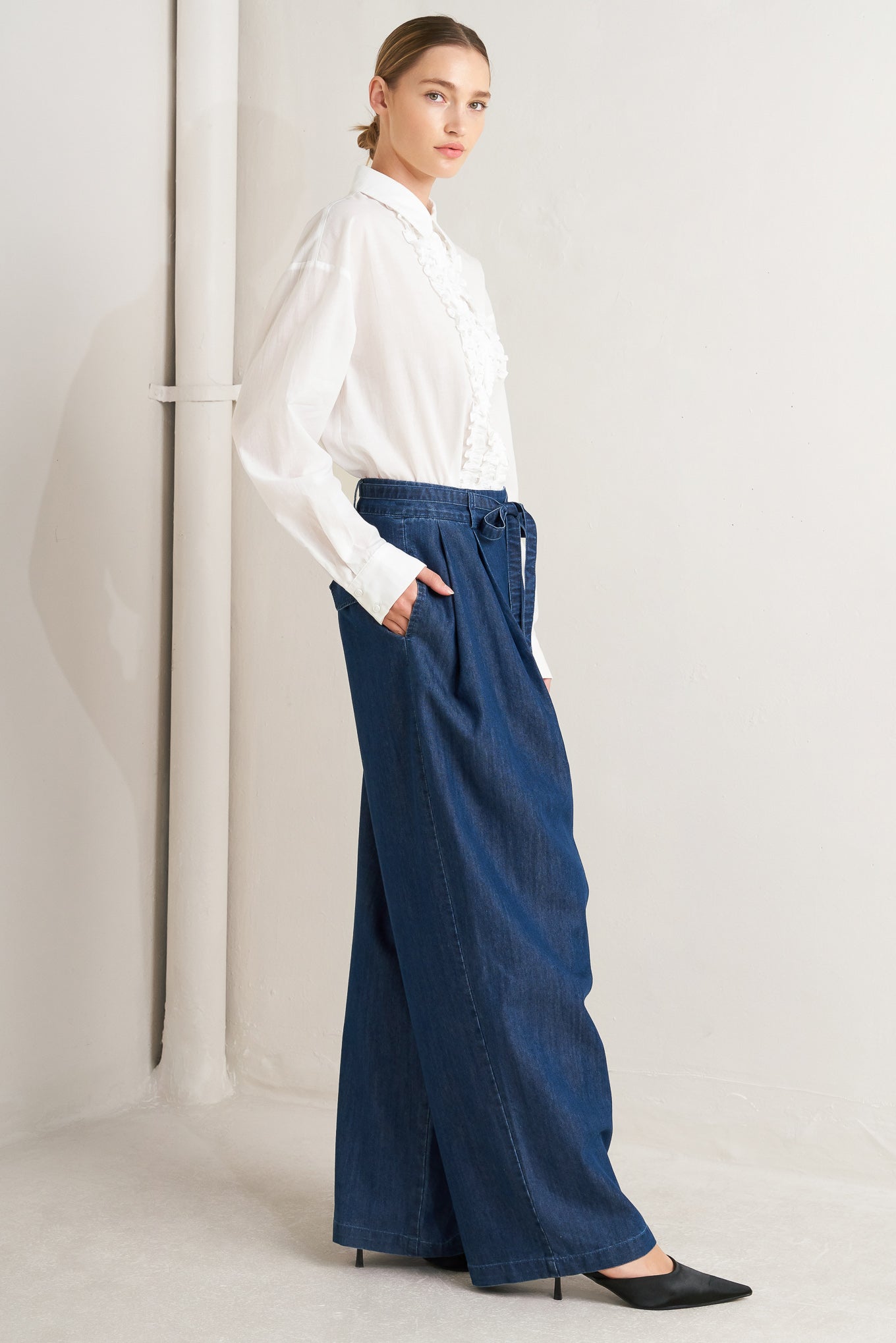 A washed denim loose fitting pant featuring crossover waistband, self sash tie, side pockets and wide leg