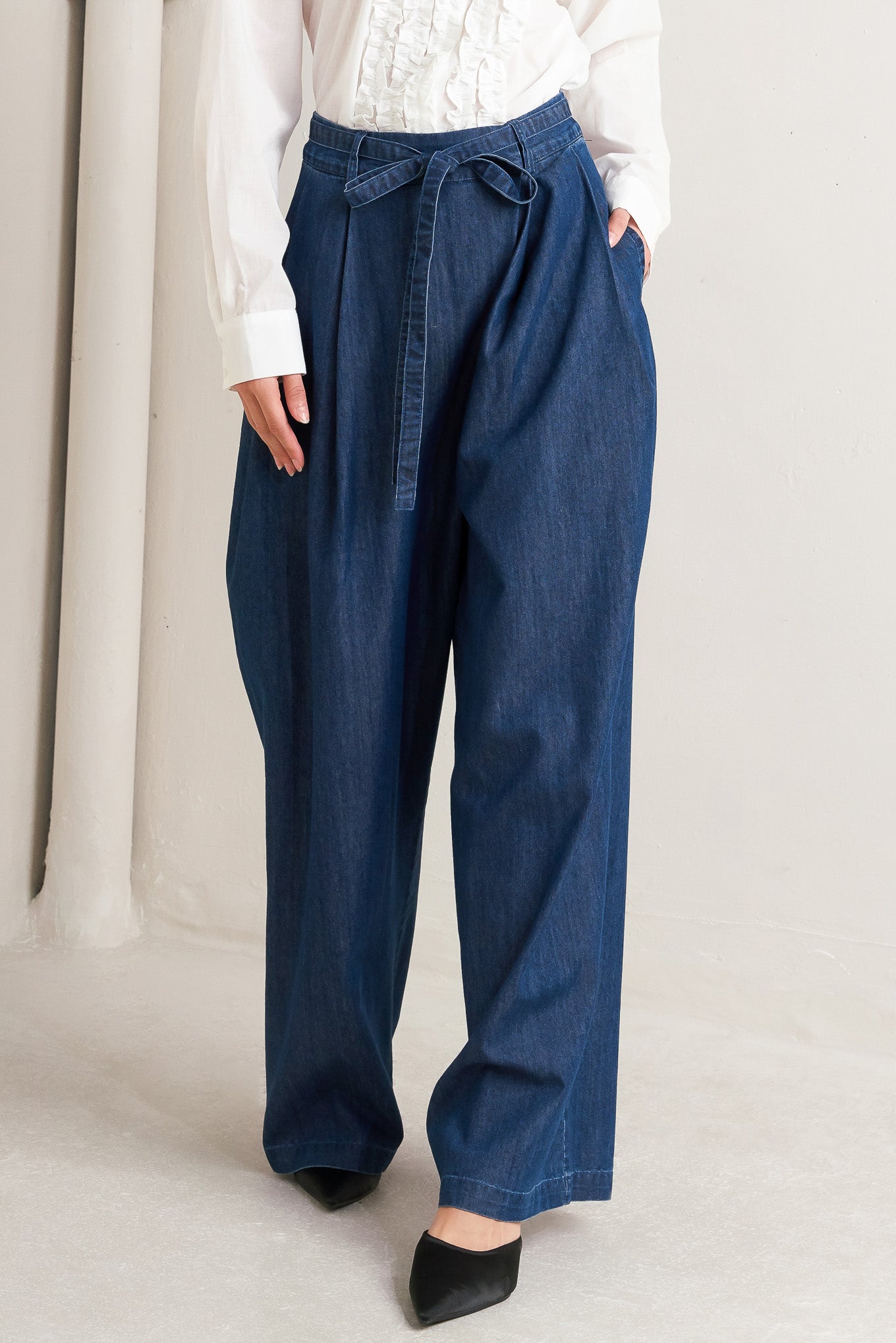 A washed denim loose fitting pant featuring crossover waistband, self sash tie, side pockets and wide leg