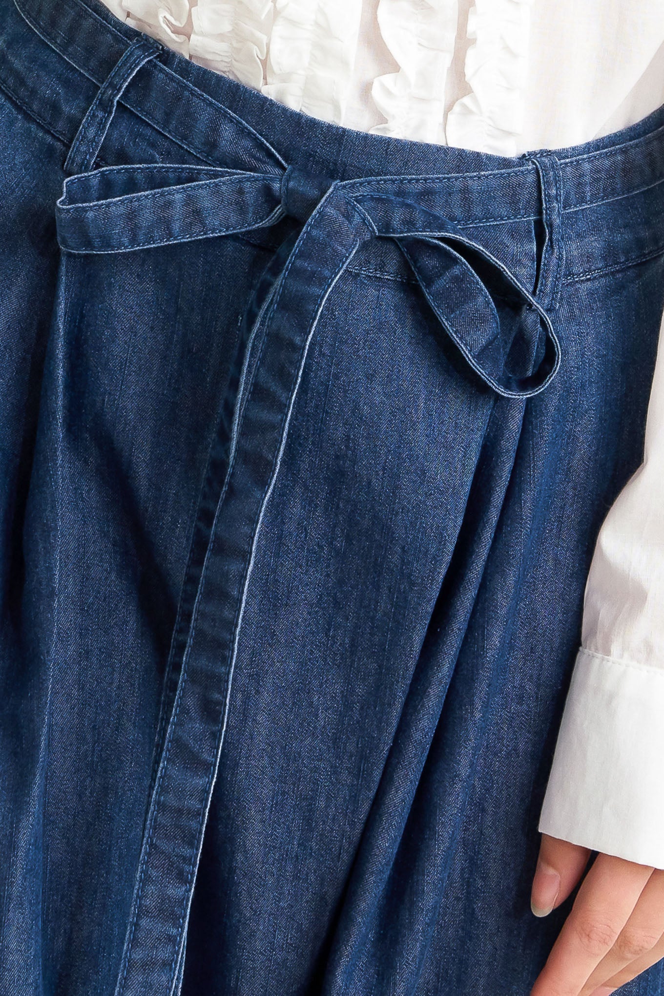 A washed denim loose fitting pant featuring crossover waistband, self sash tie, side pockets and wide leg