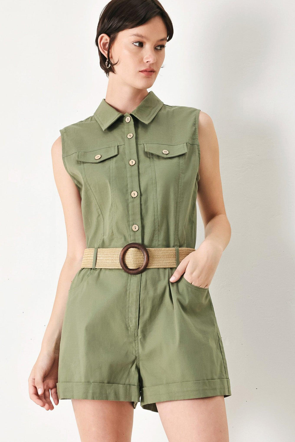 A solid woven romper featuring collar, sleeveless, front button zipper closure, pockets, cuffed hem and contrasting belt