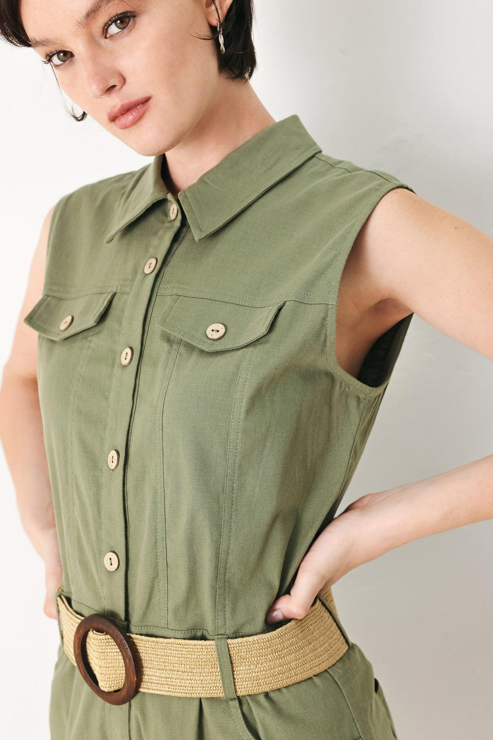 A solid woven romper featuring collar, sleeveless, front button zipper closure, pockets, cuffed hem and contrasting belt