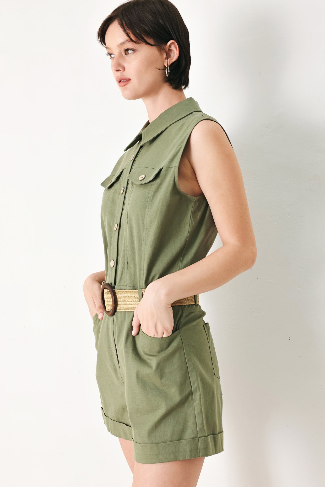 A solid woven romper featuring collar, sleeveless, front button zipper closure, pockets, cuffed hem and contrasting belt