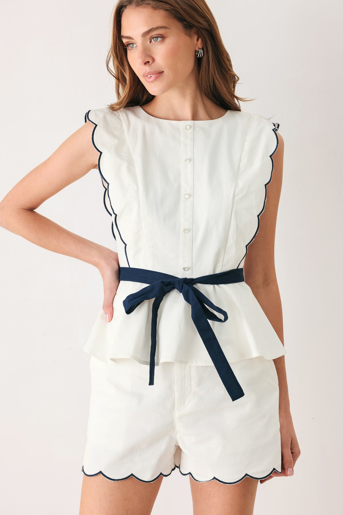 Woman wearing white shorts with scalloped hem on a plain background | FREEMARKET