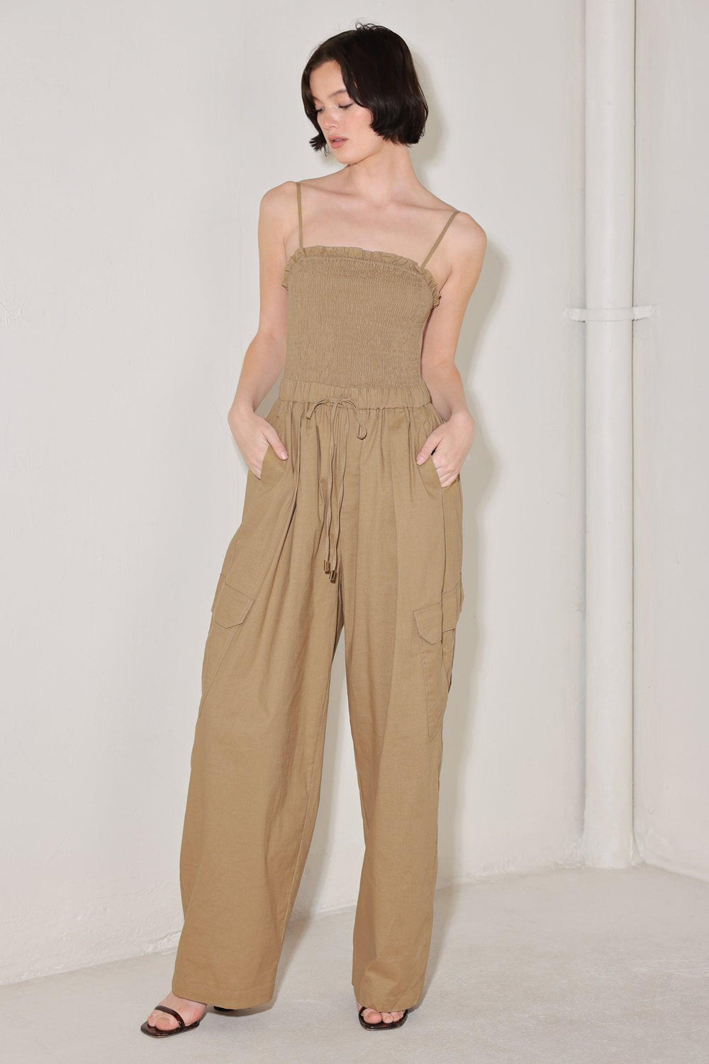 
A solid woven jumpsuit featuring straight neckline with ruffle edge, straps, smocked bodice, elastic waist with tie, pockets and wide leg

Details:

Self : 95% Cotton 5% Spandex

Size &amp; Fit

- Model is 5`8" And Wearing Size Small
- Measurements Taken From Size Small
- Approx. Length: 59"