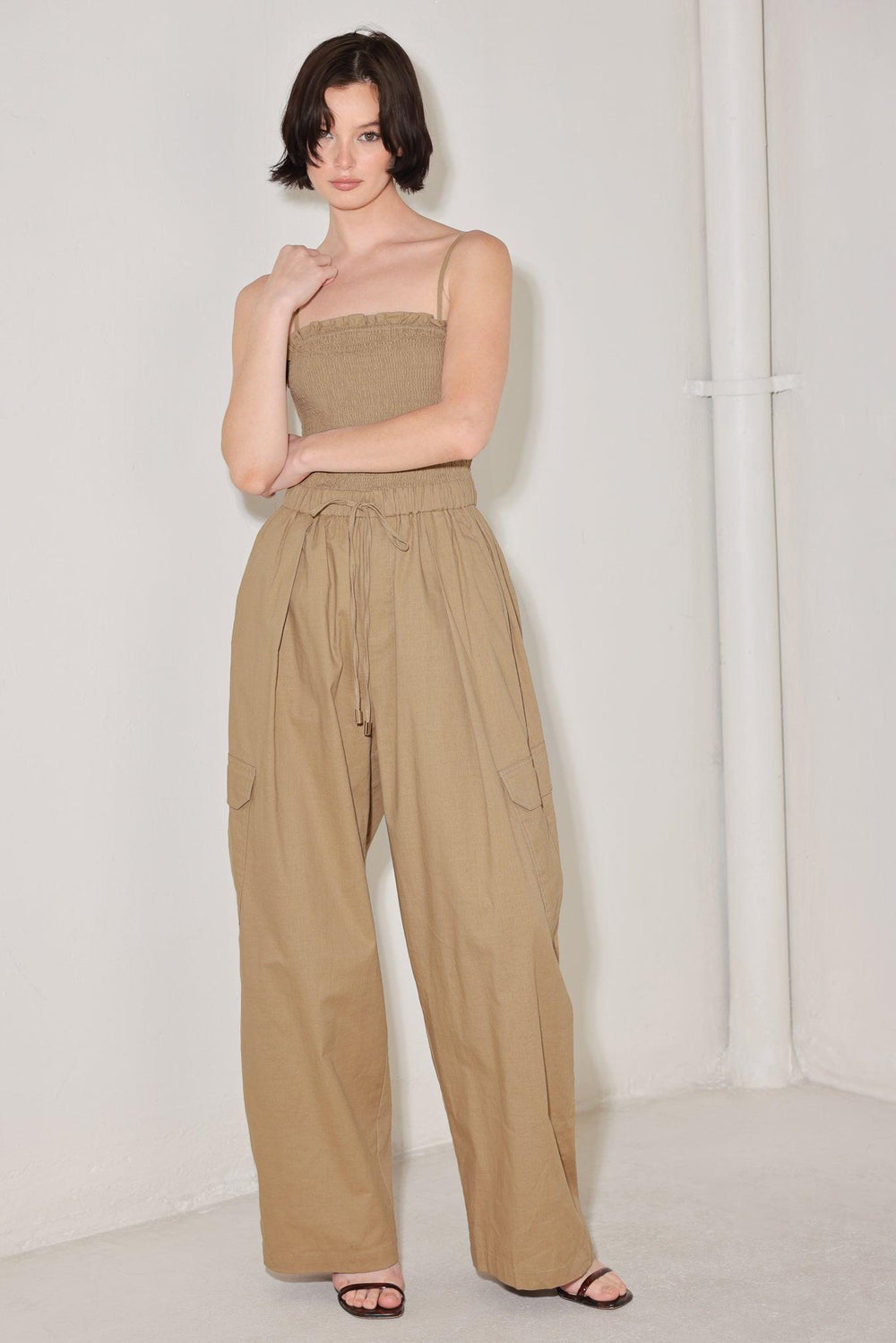 
A solid woven jumpsuit featuring straight neckline with ruffle edge, straps, smocked bodice, elastic waist with tie, pockets and wide leg

Details:

Self : 95% Cotton 5% Spandex

Size &amp; Fit

- Model is 5`8" And Wearing Size Small
- Measurements Taken From Size Small
- Approx. Length: 59"