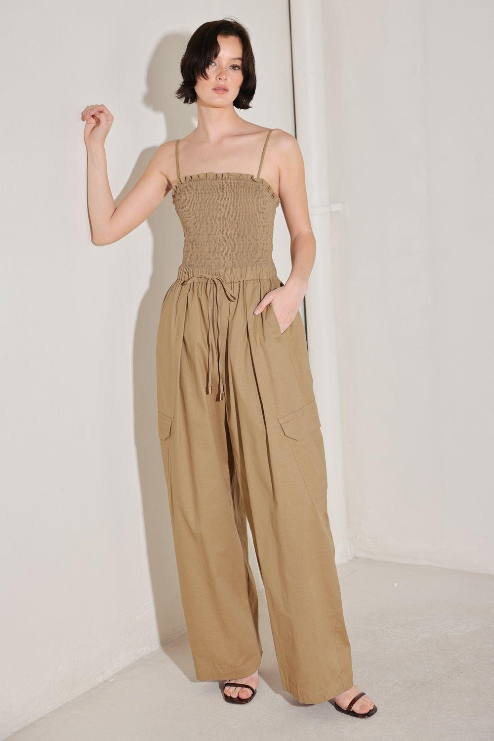 
A solid woven jumpsuit featuring straight neckline with ruffle edge, straps, smocked bodice, elastic waist with tie, pockets and wide leg

Details:

Self : 95% Cotton 5% Spandex

Size &amp; Fit

- Model is 5`8" And Wearing Size Small
- Measurements Taken From Size Small
- Approx. Length: 59"