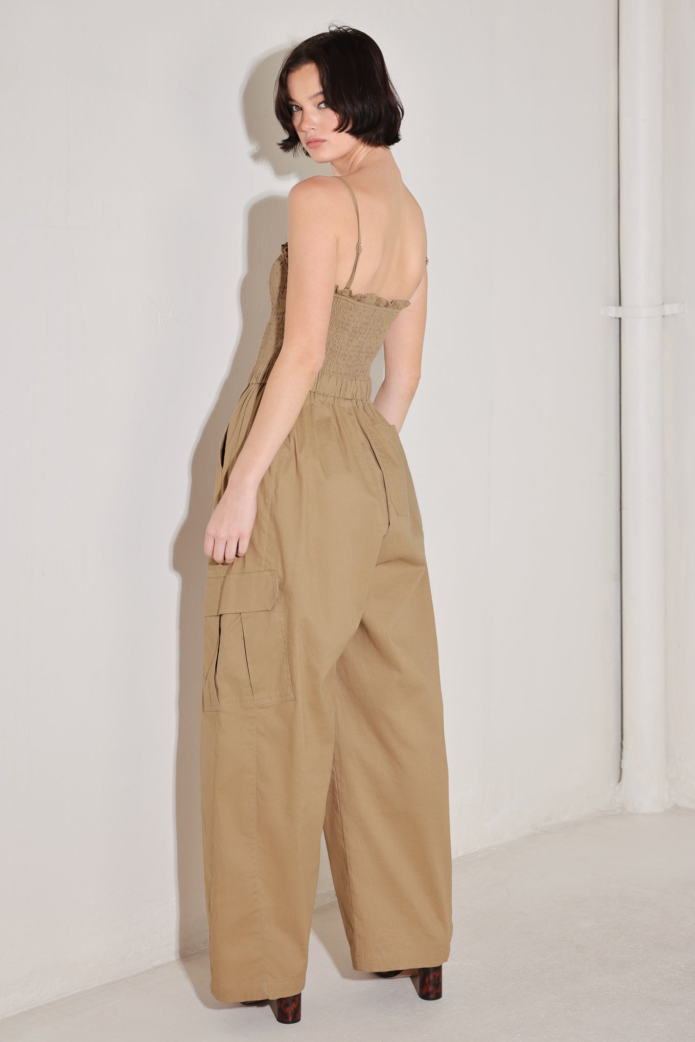 
A solid woven jumpsuit featuring straight neckline with ruffle edge, straps, smocked bodice, elastic waist with tie, pockets and wide leg

Details:

Self : 95% Cotton 5% Spandex

Size &amp; Fit

- Model is 5`8" And Wearing Size Small
- Measurements Taken From Size Small
- Approx. Length: 59"