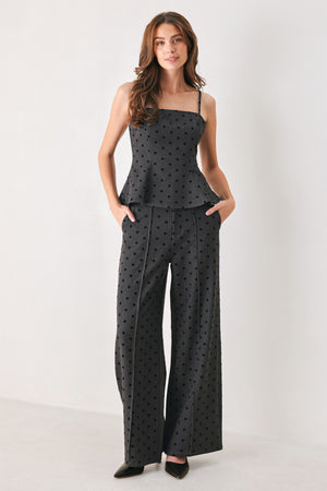 Woman wearing a pair of high waisted charcoal trousers with black polka dots | FREEMARKET