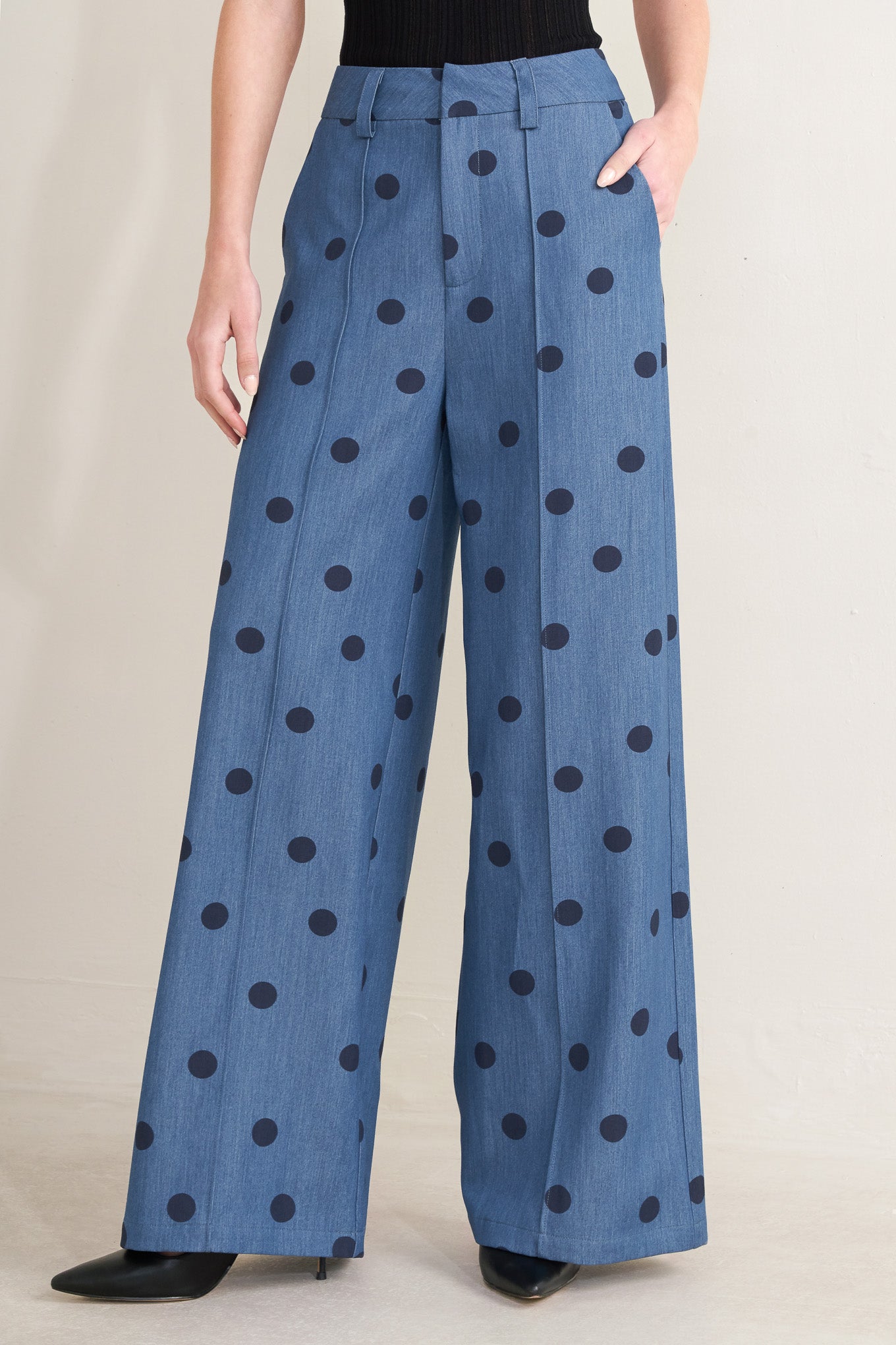 Blue pants with black polka dots worn by a person on a beige background