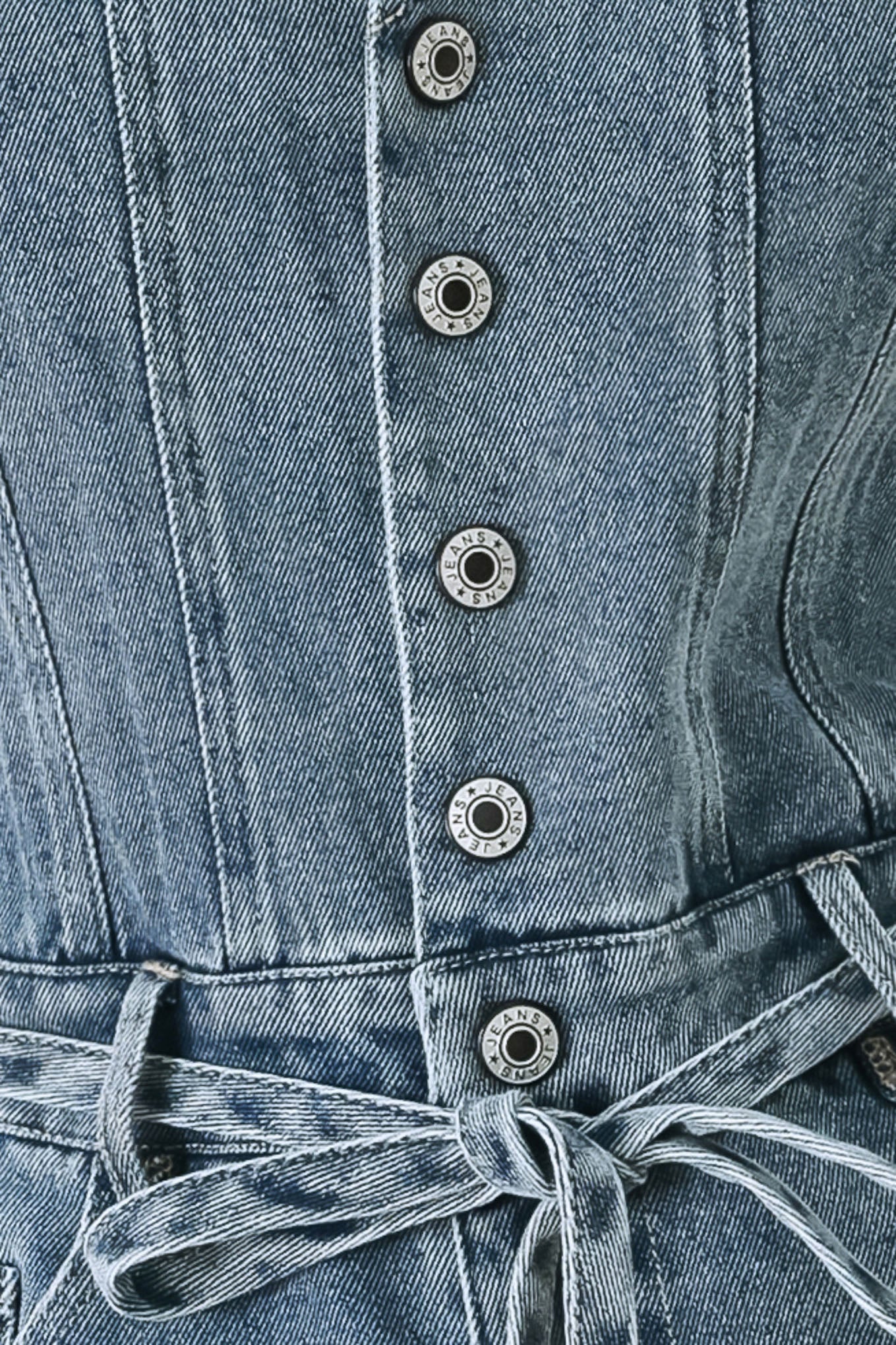 A washed denim romper featuring V neckline, sleeveless, front button/zipper closure, pockets and skinny waist tie