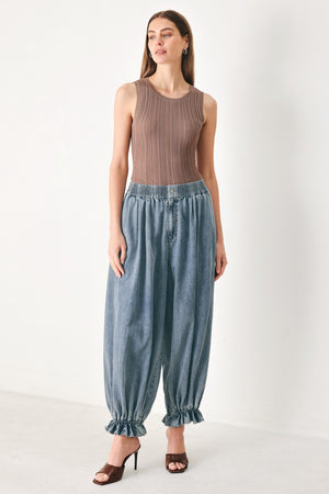 Woman wearing light blue denim genie pants with elastic waist, front closure and side pockets | FREEMARKET | Flying Tomato