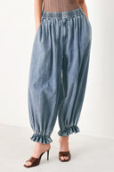 Woman wearing light blue denim genie pants with elastic waist, front closure and side pockets | FREEMARKET | Flying Tomato