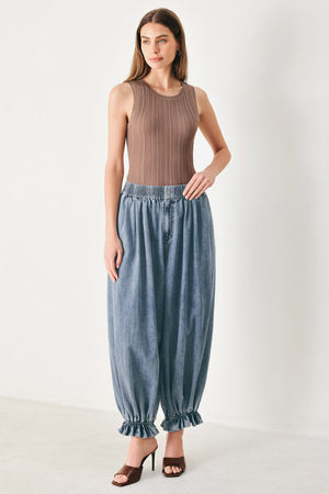 Woman wearing light blue denim genie pants with elastic waist, front closure and side pockets | FREEMARKET | Flying Tomato