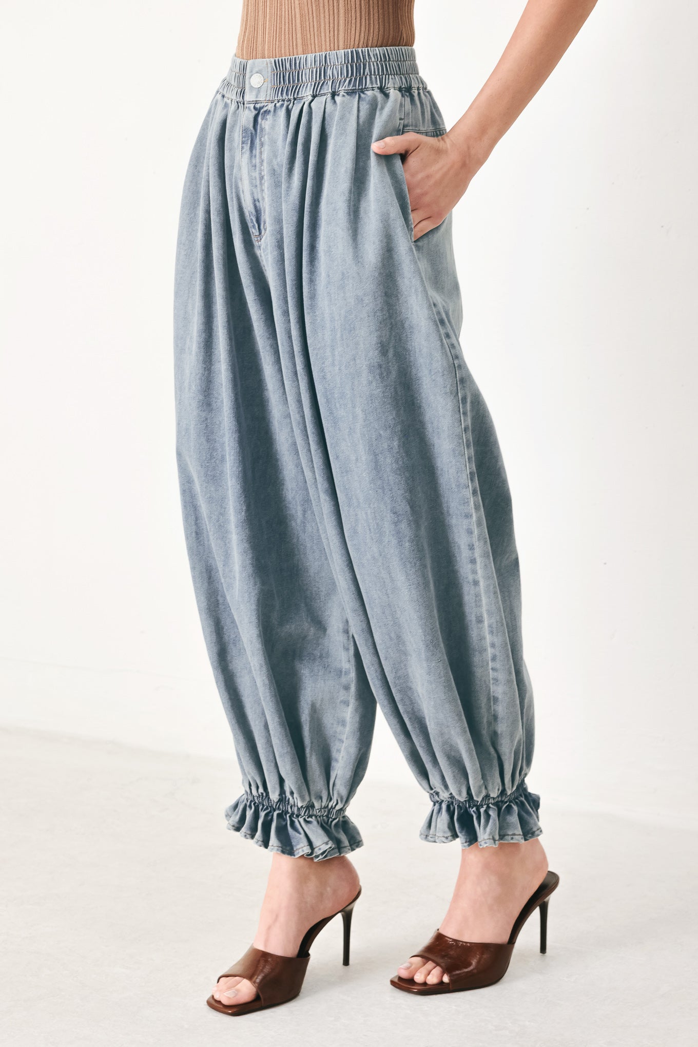 Woman wearing light blue denim genie pants with elastic waist, front closure and side pockets | FREEMARKET | Flying Tomato
