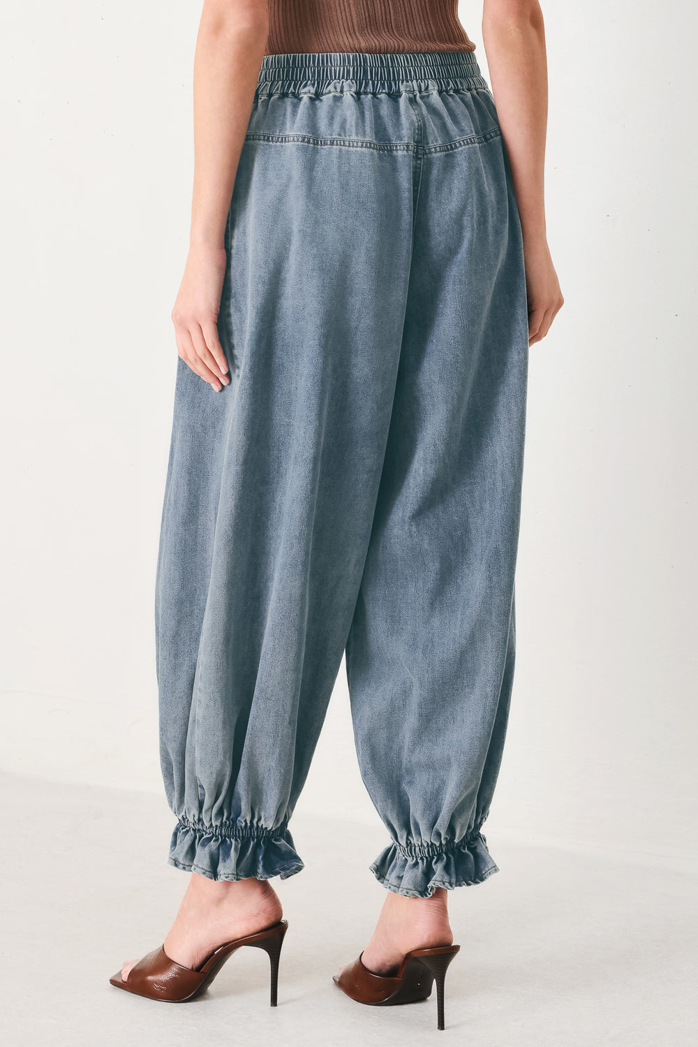 Woman wearing light blue denim genie pants with elastic waist, front closure and side pockets | FREEMARKET | Flying Tomato