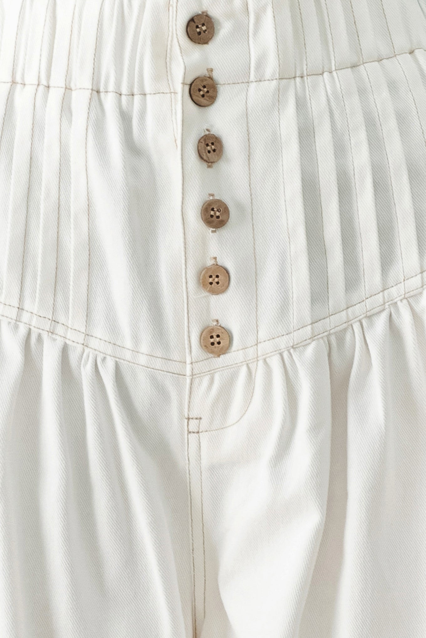 Close up of a white solid woven pant with elastic waist band, front button closure, pintuck detail and wide leg | FREEMARKET
