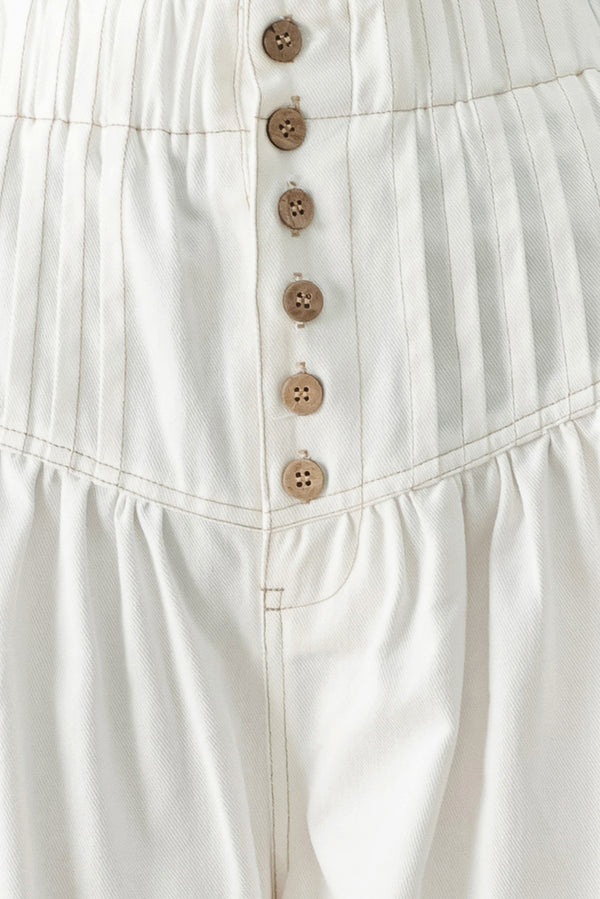 Close up of a white solid woven pant with elastic waist band, front button closure, pintuck detail and wide leg | FREEMARKET