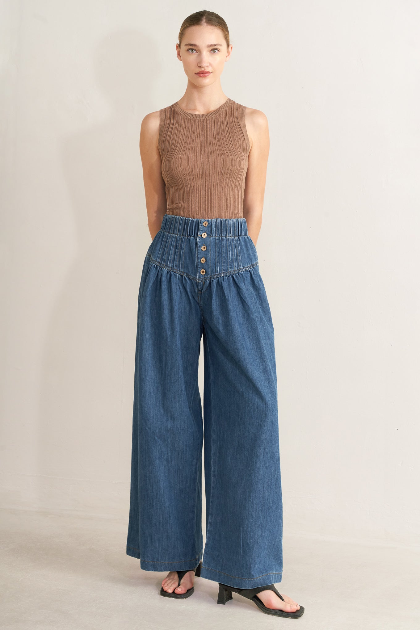 Woman wearing a brown sleeveless top and blue wide-leg pants on a beige background