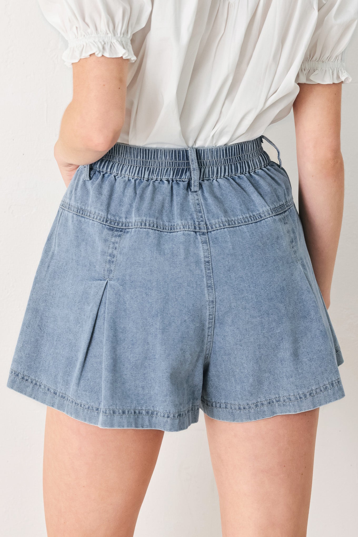 Woman wearing washed light denim short featuring elastic waist, front closure, front pockets and pleats with wide leg | FREEMARKET
