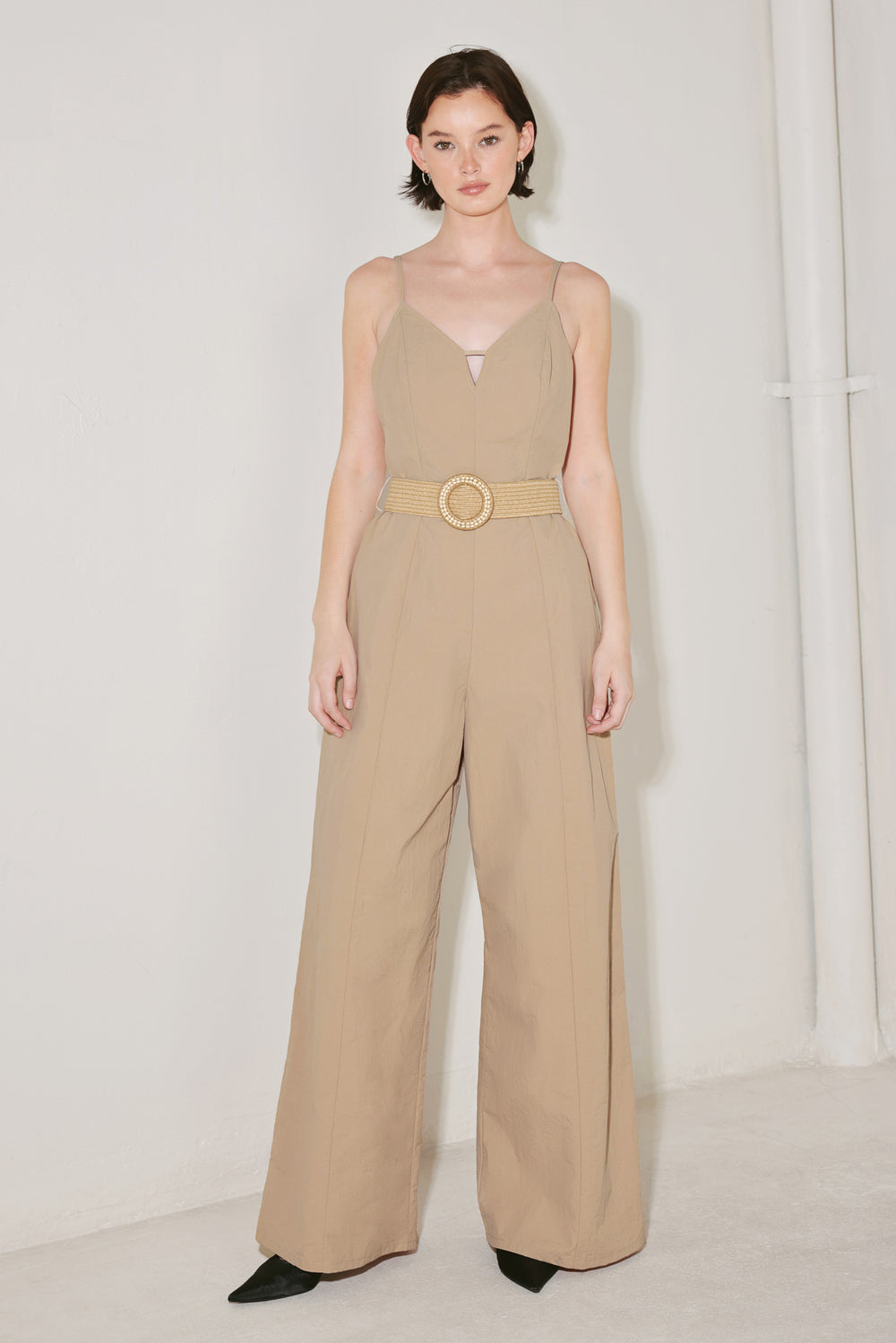 Woman wearing a beige jumpsuit featuring cami top, straps, contrasting belt, wide leg and back zipper closure | FREEMARKET | Flying Tomato