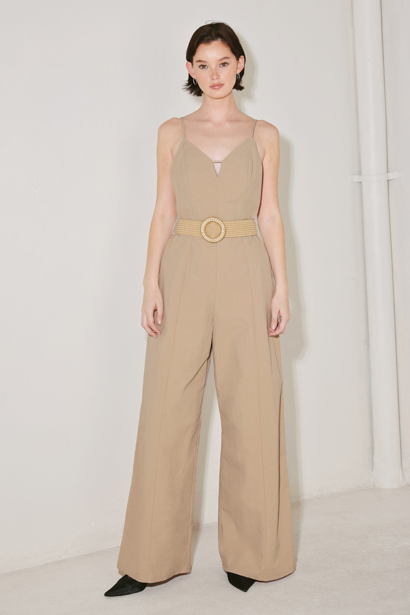 Woman wearing a beige jumpsuit featuring cami top, straps, contrasting belt, wide leg and back zipper closure | FREEMARKET | Flying Tomato